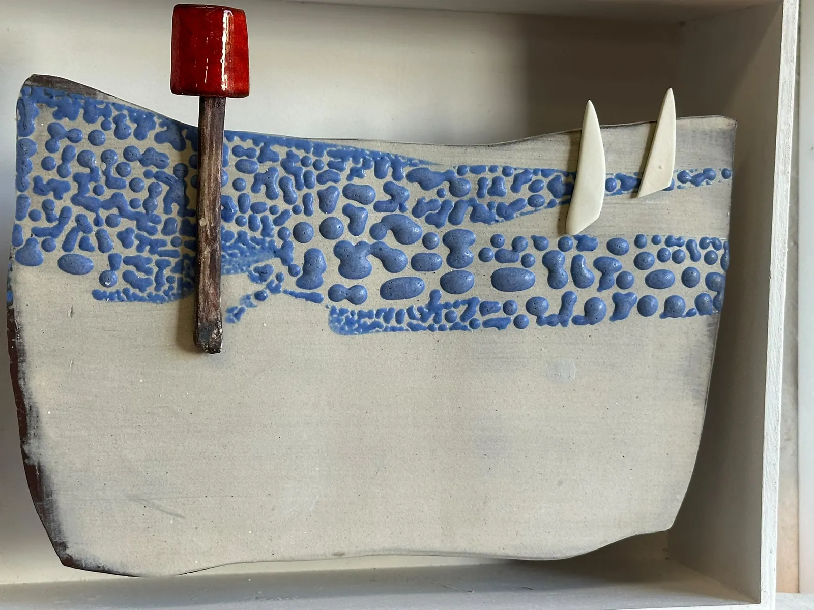 Blue and cream ceramic seascape with two white sails and a red navigation marker, by Pat Todd