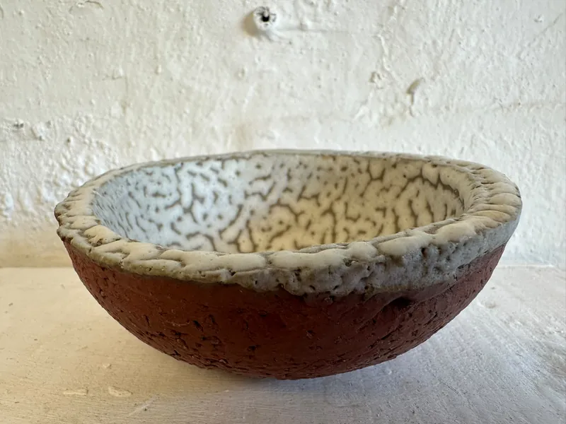 Rust-coloured ceramic bowl with a cream crackle-glazed interior and softly irregular rim
